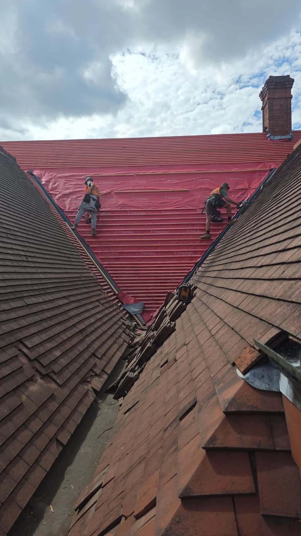 Roofer repairing tiles on a pitched roof under a cloudy sky