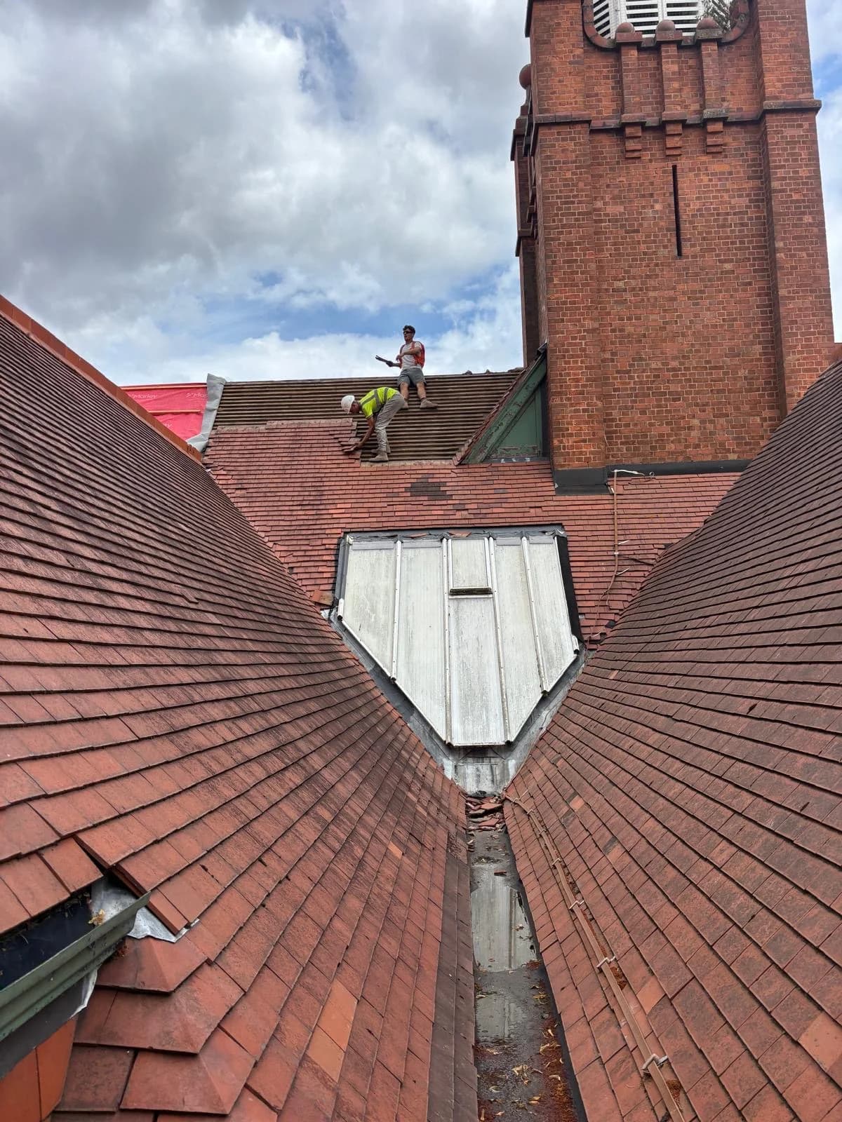 Roofer working on a tiled roof ridge beside a tall chimney stack